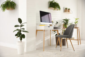 Modern workplace in room decorated with green potted plants.